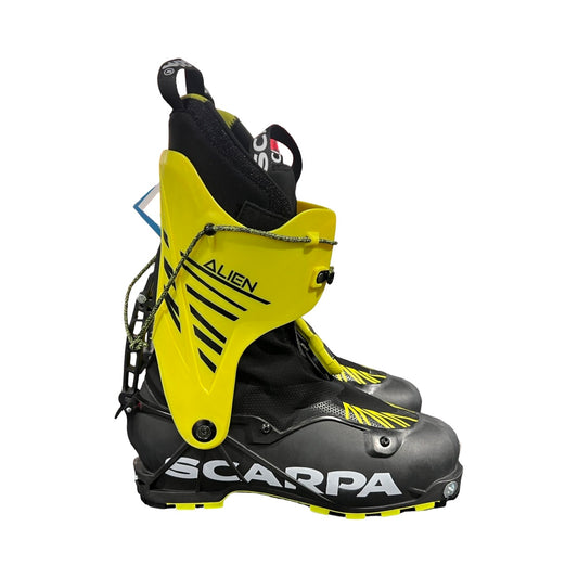 Ett par Scarpa Alien Carbon Grimalid pjäxor för herr i svart och gult, fotograferade snett från sidan mot en vit bakgrund.