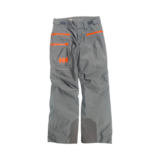 Helly Hansen Garibaldi skidbyxa för herr i mörkgrått med orangea dragkedjor, fotograferad platt mot en vit bakgrund.