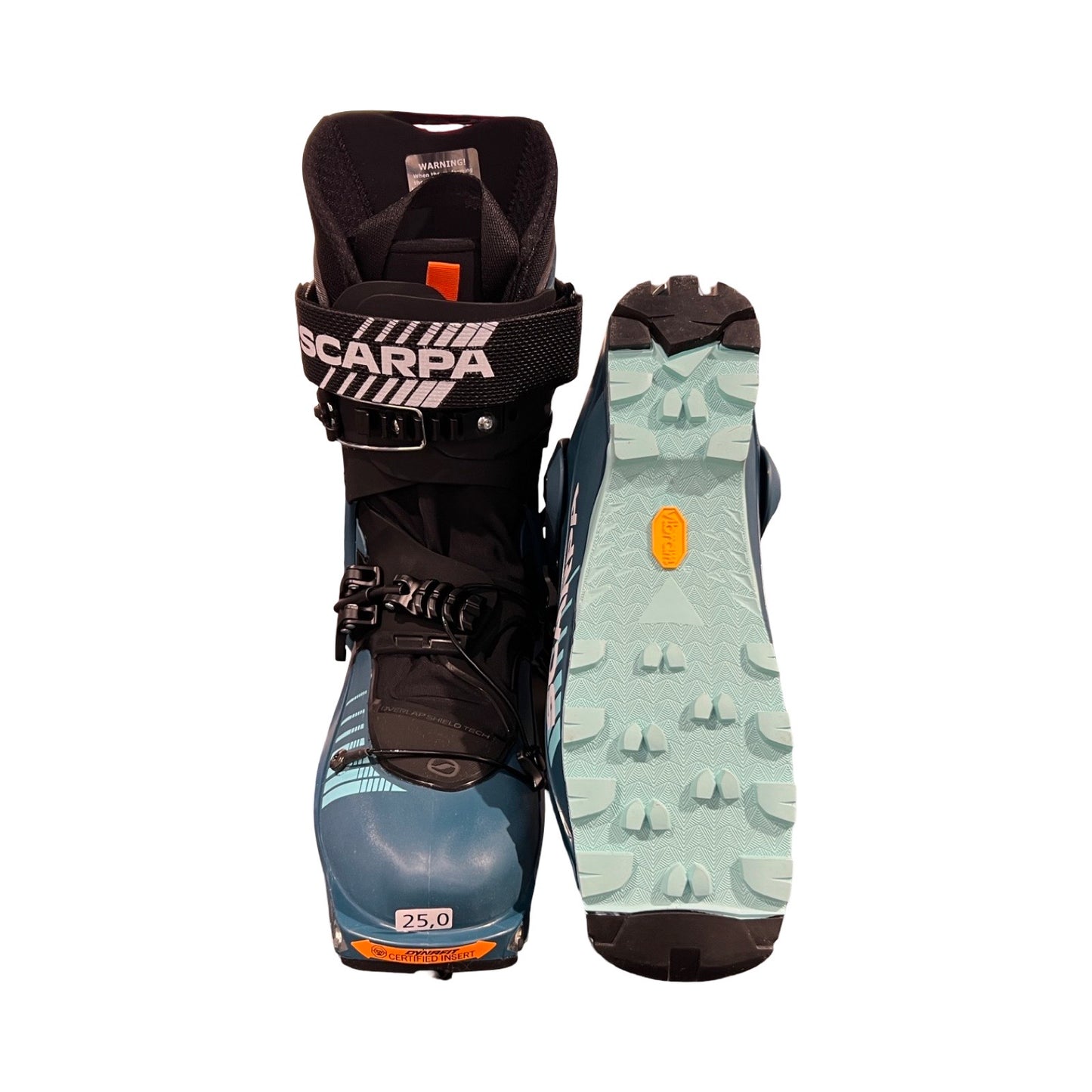 Ett par Scarpa F1 GT pjäxor för dam i blått och turkost, fotograferade mot en vit bakgrund. Ena pjäxan visas framifrån och den andra visar sulan.