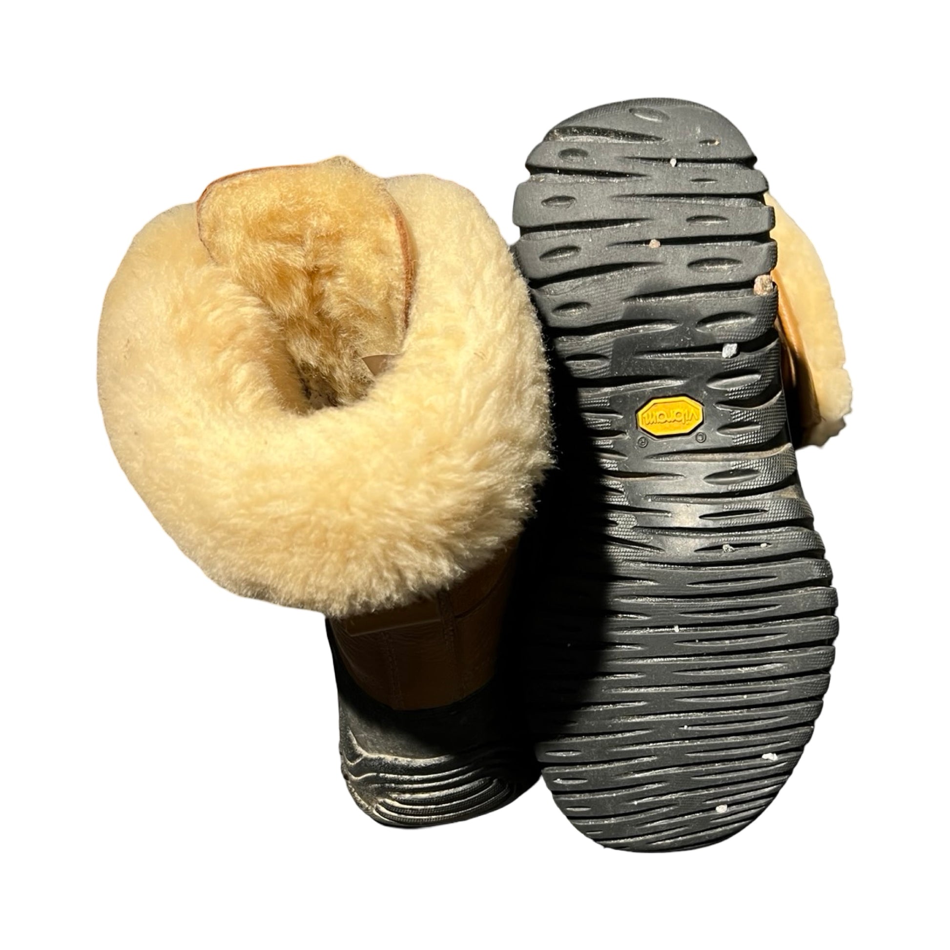Undersidan och öppningen på ett par bruna UGG vinterkängor för dam. Bilden visar den svarta Vibram-sulan och det tjocka, ljusa fodret mot en vit bakgrund.