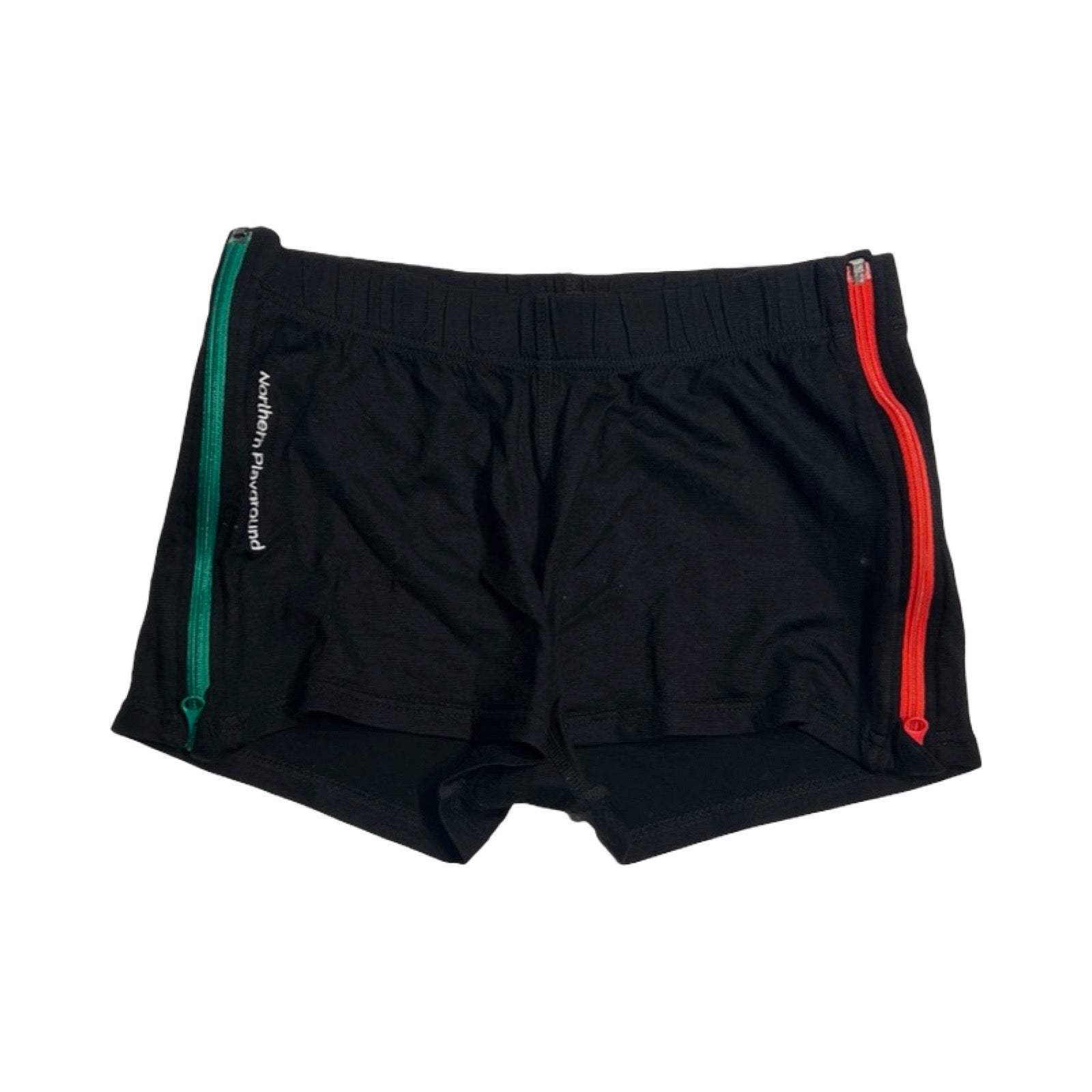 Underställsshorts från Northern Playground för dam i svart merinoull. Shortsen har sidodragkedjor i grönt och rött och är fotograferade platt mot en vit bakgrund.