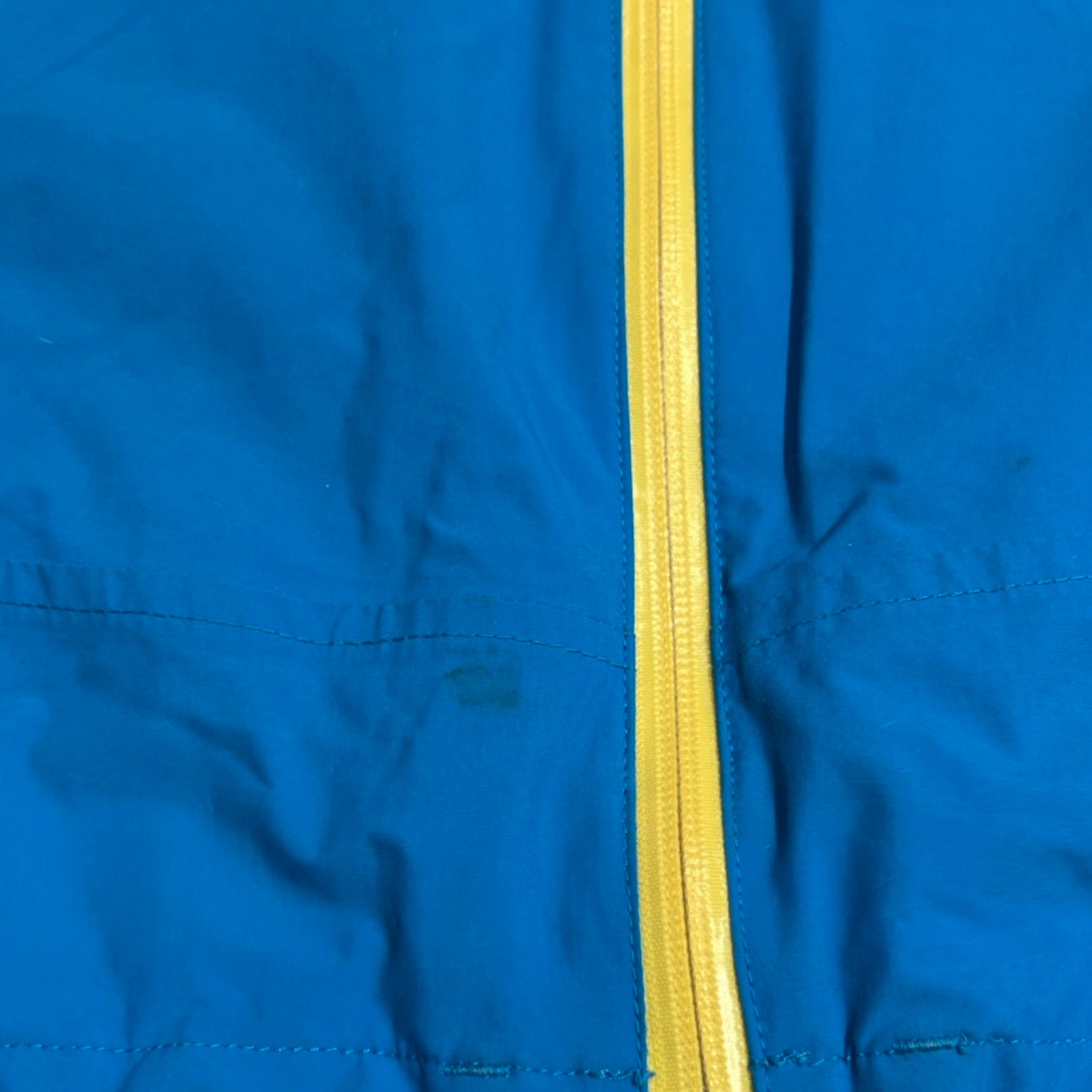 Närbild på en fläck på den blå skaljackan från The North Face för dam, bredvid den gula dragkedjan.