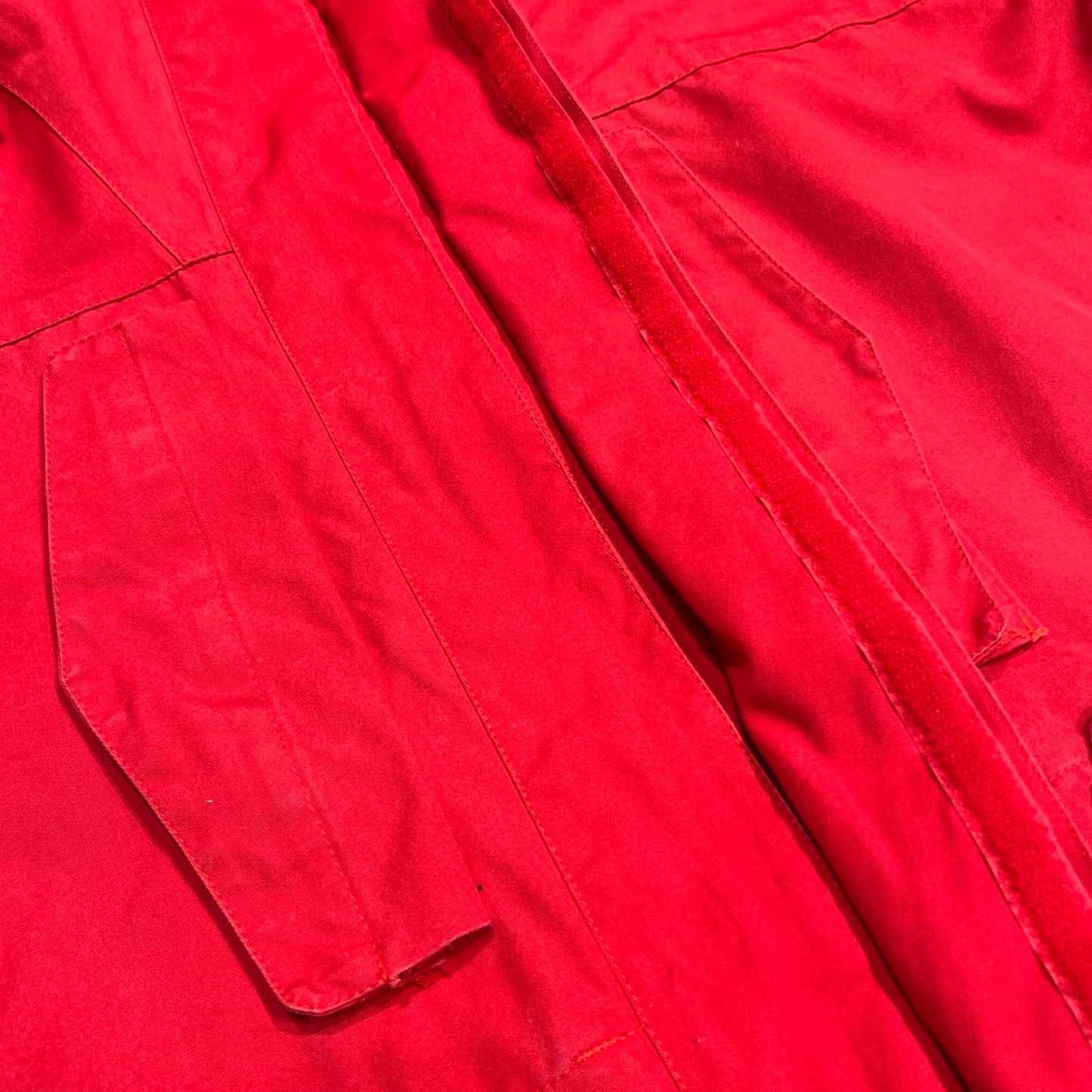 Detaljbild av den röda Norröna Arktis Anojakke för dam. Bilden visar en ficka och stormslån med skadat kardborreband.