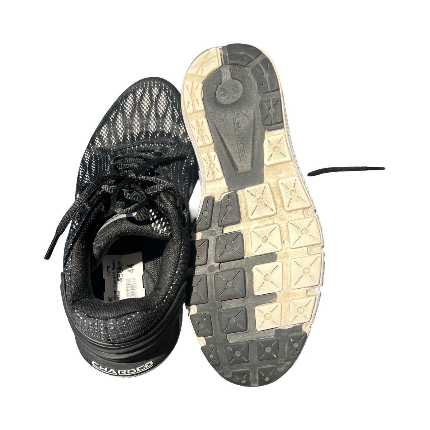 Ett par Under Armour Charged träningsskor i svart. Bilden visar ena skon ovanifrån och den andra skons sula, fotograferade mot en vit bakgrund.