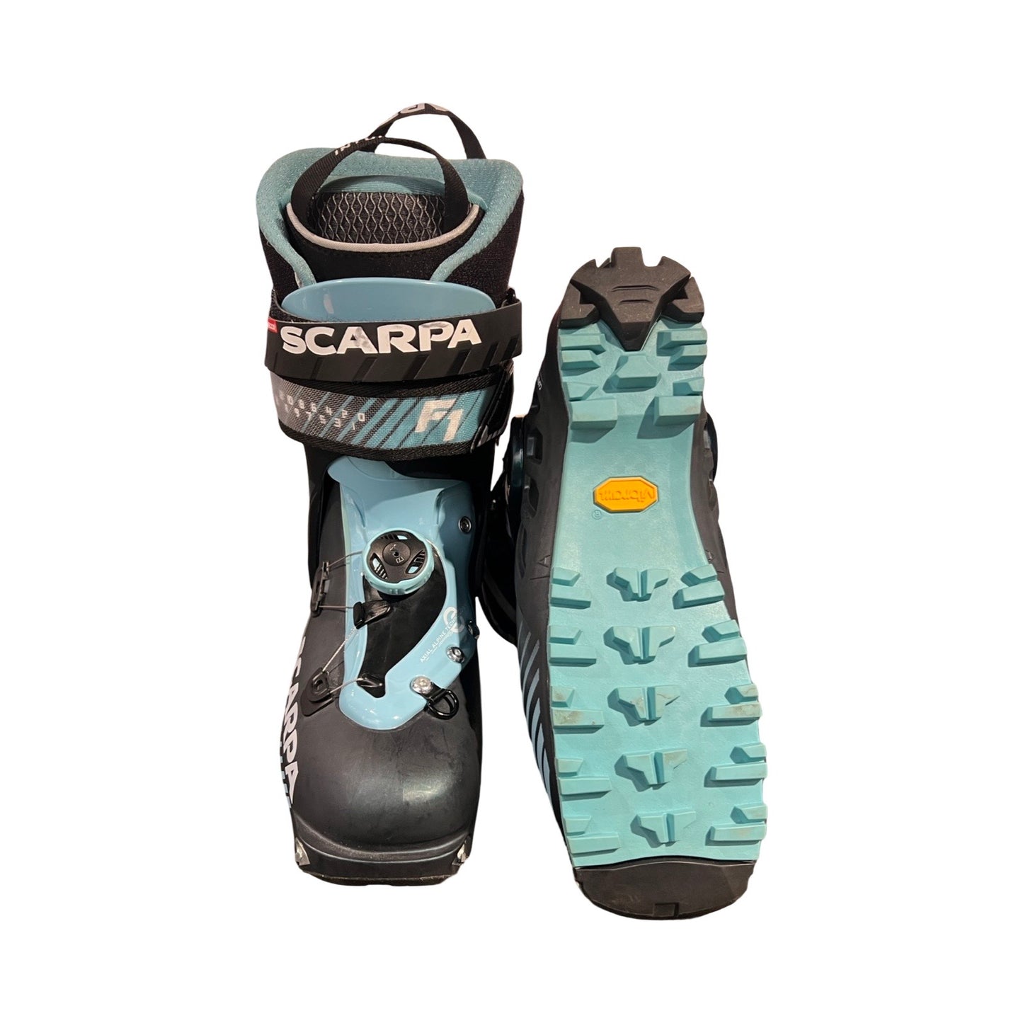 Ett par Scarpa F1-pjäxor för dam i svart och ljusblått, där ena pjäxan visas framifrån och den andra visar sulan. Fotograferade mot en vit bakgrund.