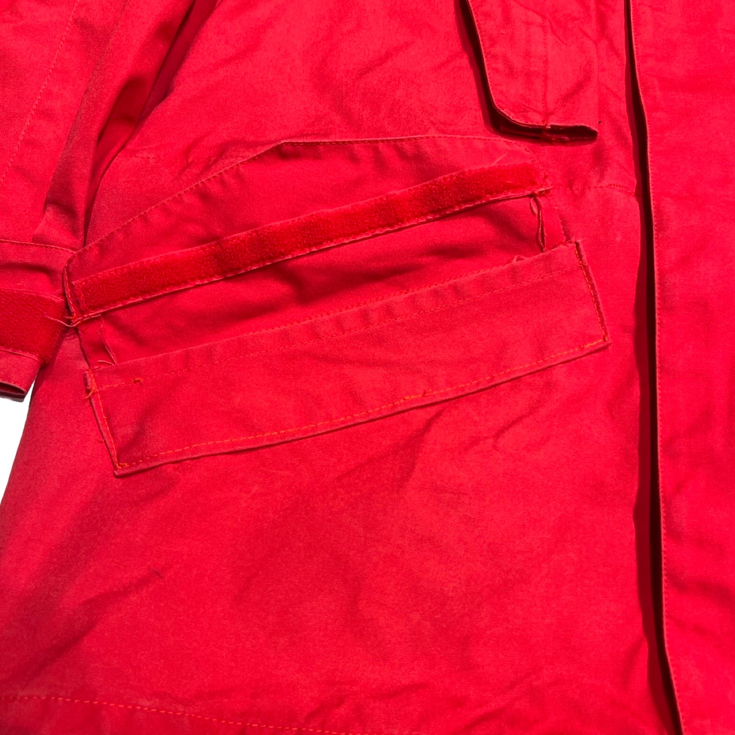 Närbild av en ficka på Norröna Arktis Anojakke för dam i rött, som visar att ena delen av kardborrebandet saknas.