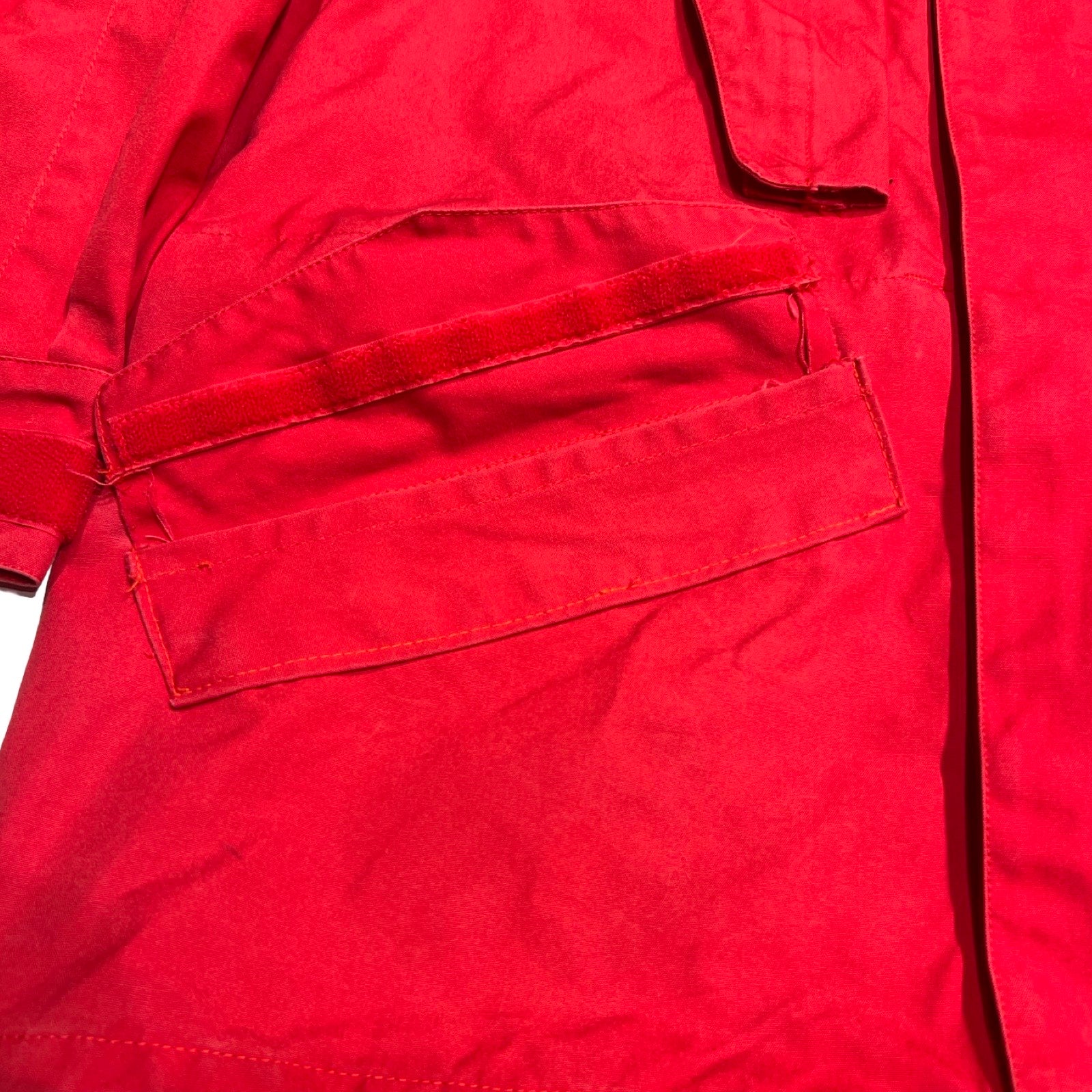 Närbild av en ficka på Norröna Arktis Anojakke för dam i rött, som visar att ena delen av kardborrebandet saknas.