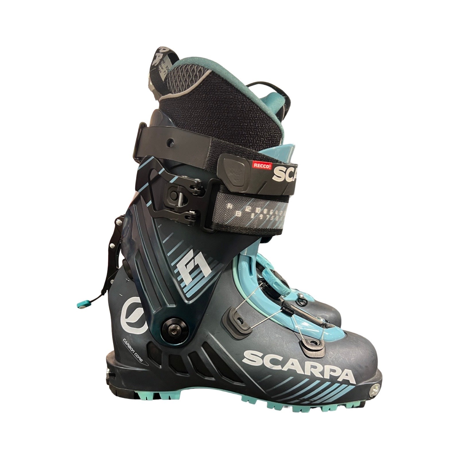 Ett par Scarpa F1 pjäxor för dam i mörkgrått och turkost, fotograferade från sidan mot en vit bakgrund.