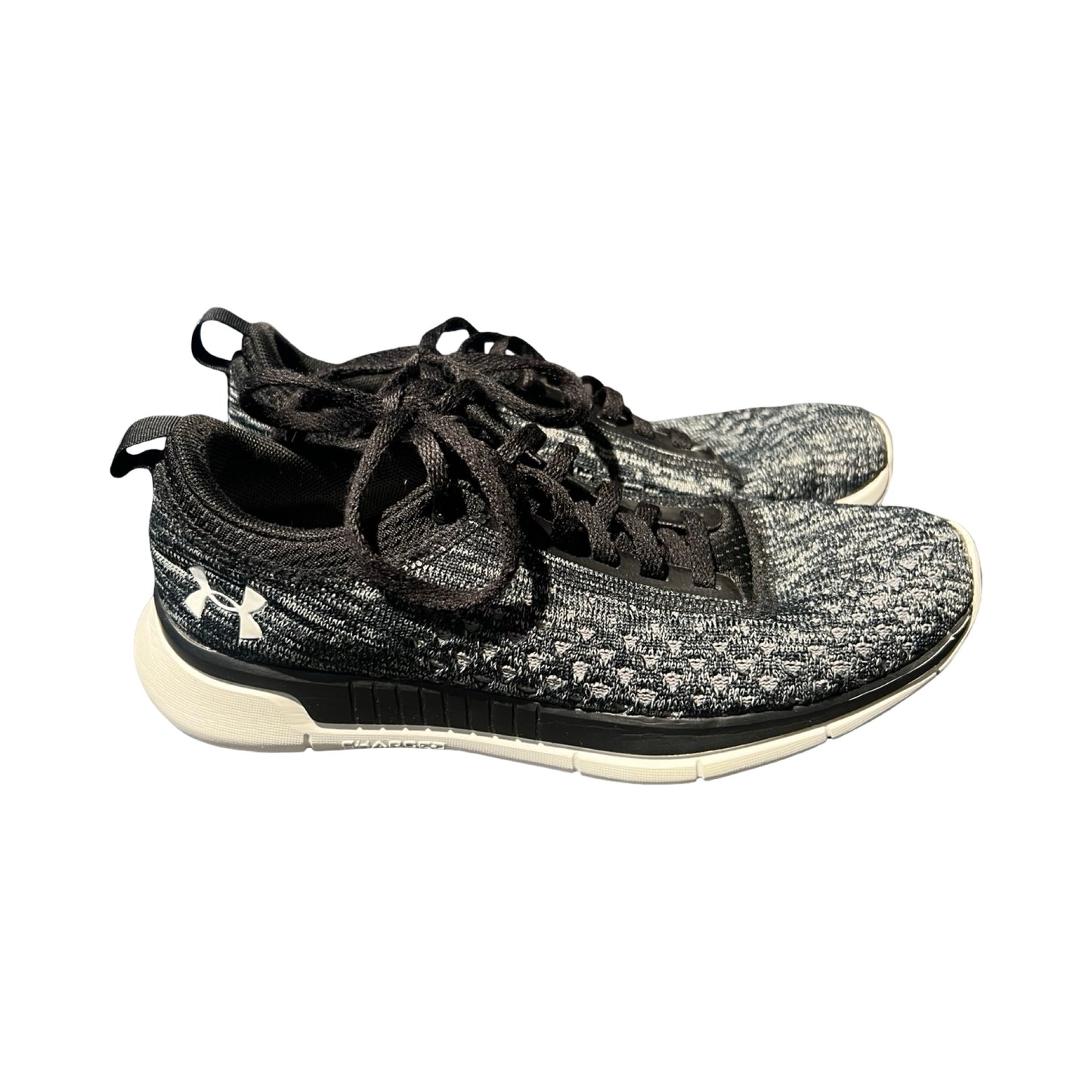 Under Armour träningsskor för dam i svart och grått, fotograferade från sidan mot en vit bakgrund.