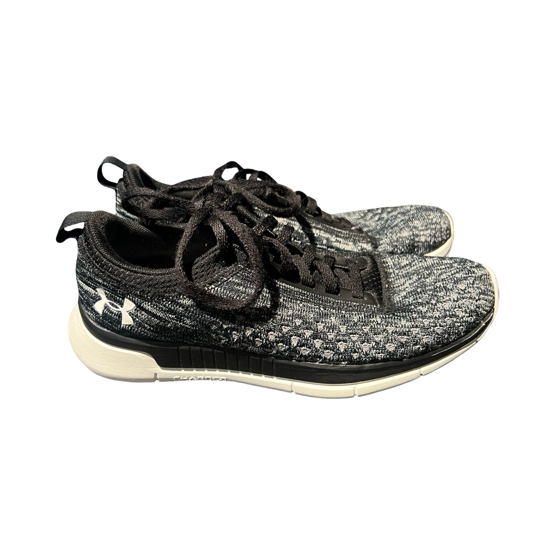 Under Armour träningsskor för dam i svart och grått, fotograferade från sidan mot en vit bakgrund.