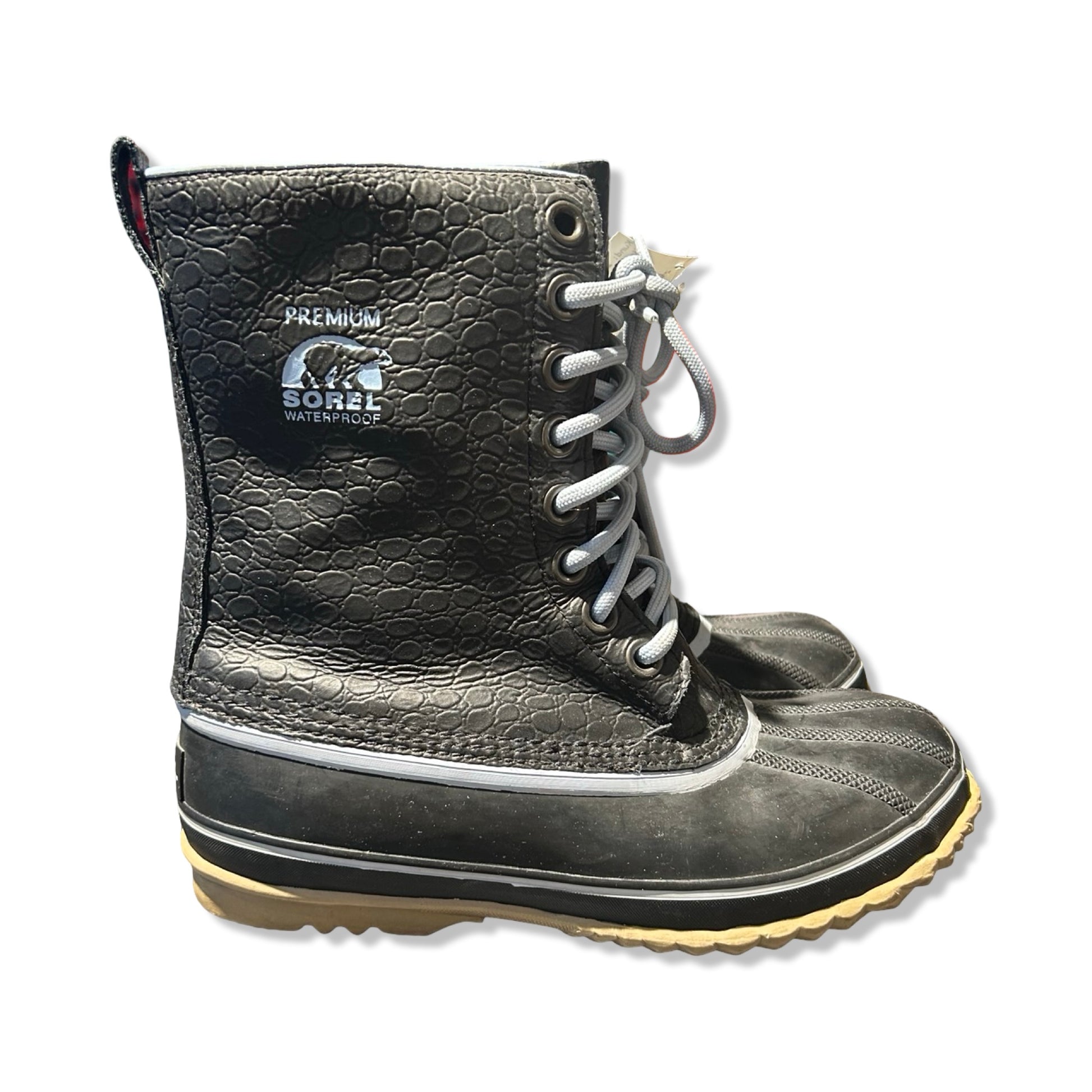 Sorel Premium vinterkängor för dam i svart med texturerat skaft och ljusgrå snörning. Kängorna är fotograferade från sidan mot en vit bakgrund.