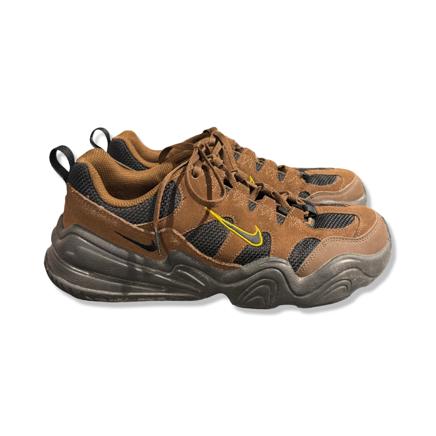 Nike Tech Hera sneakers för herr i brunt och svart med gula detaljer, fotograferade från sidan mot en vit bakgrund.