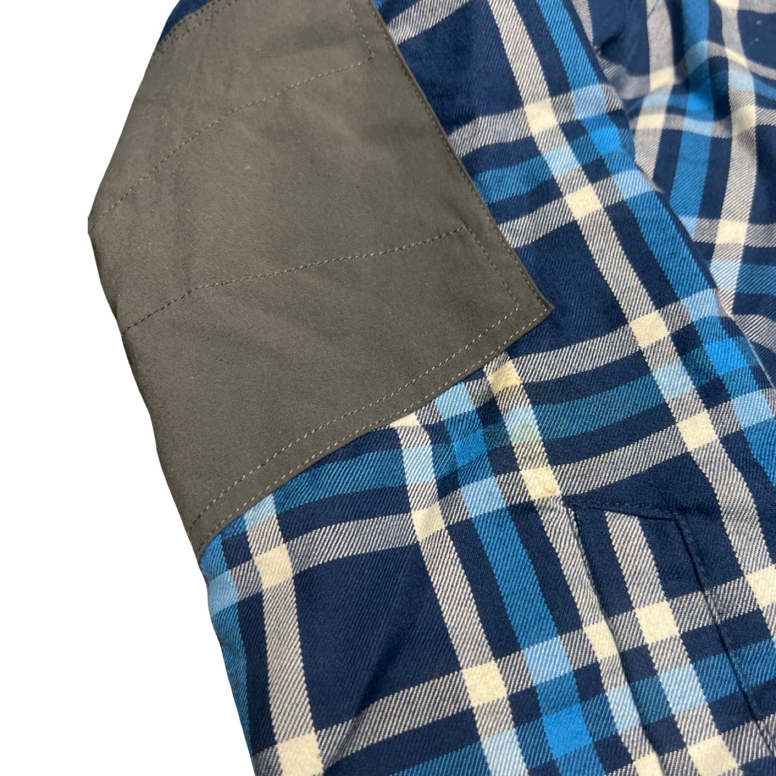 Närbild på syntetjackan Haglöfs Tundra för herr. Detaljbilden visar jackans blå- och vitrutiga tyg med en grå förstärkningspanel.