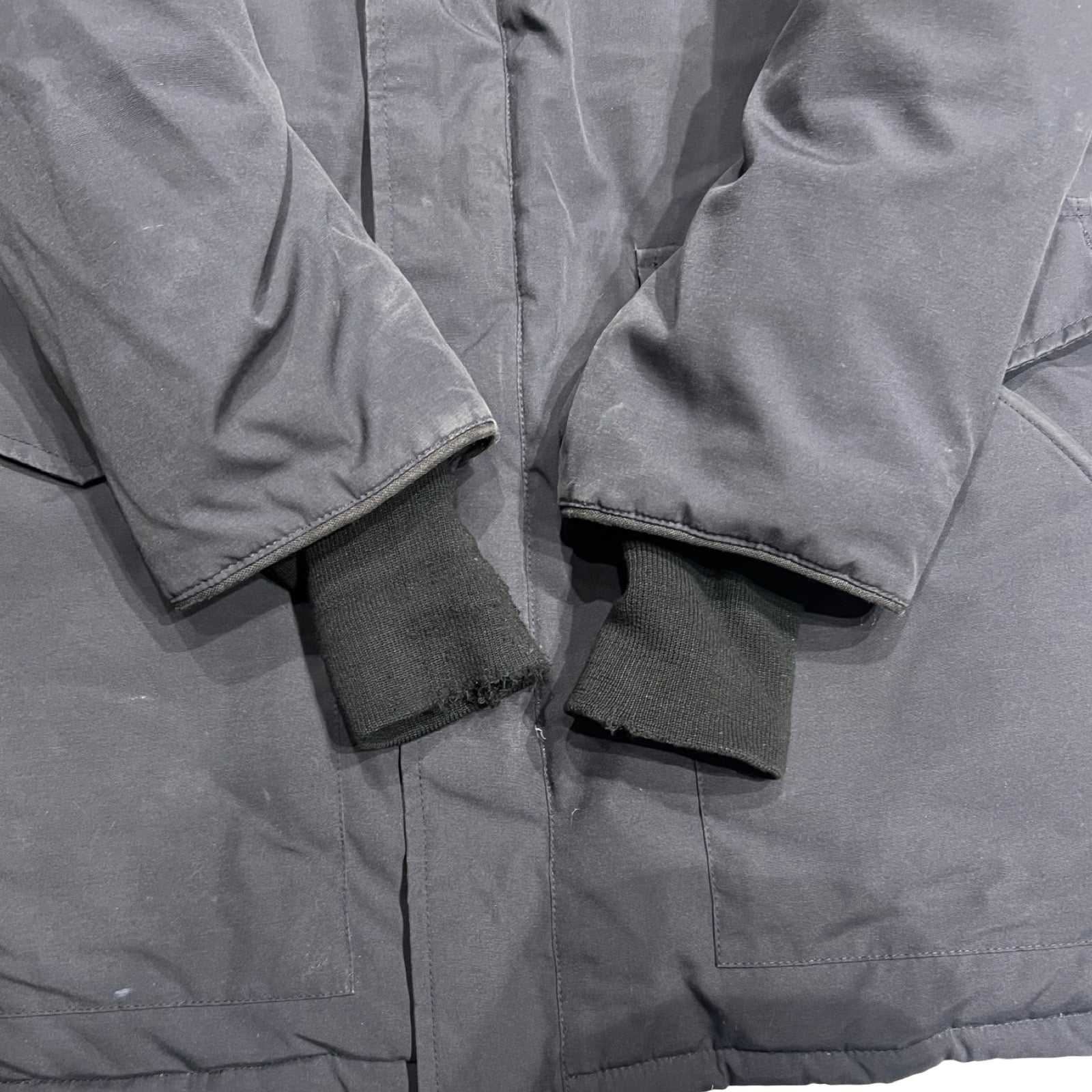 Närbild på ärmsluten av Canada Goose Heli Arctic dunjacka för herr i svart som visar slitage på muddarna.