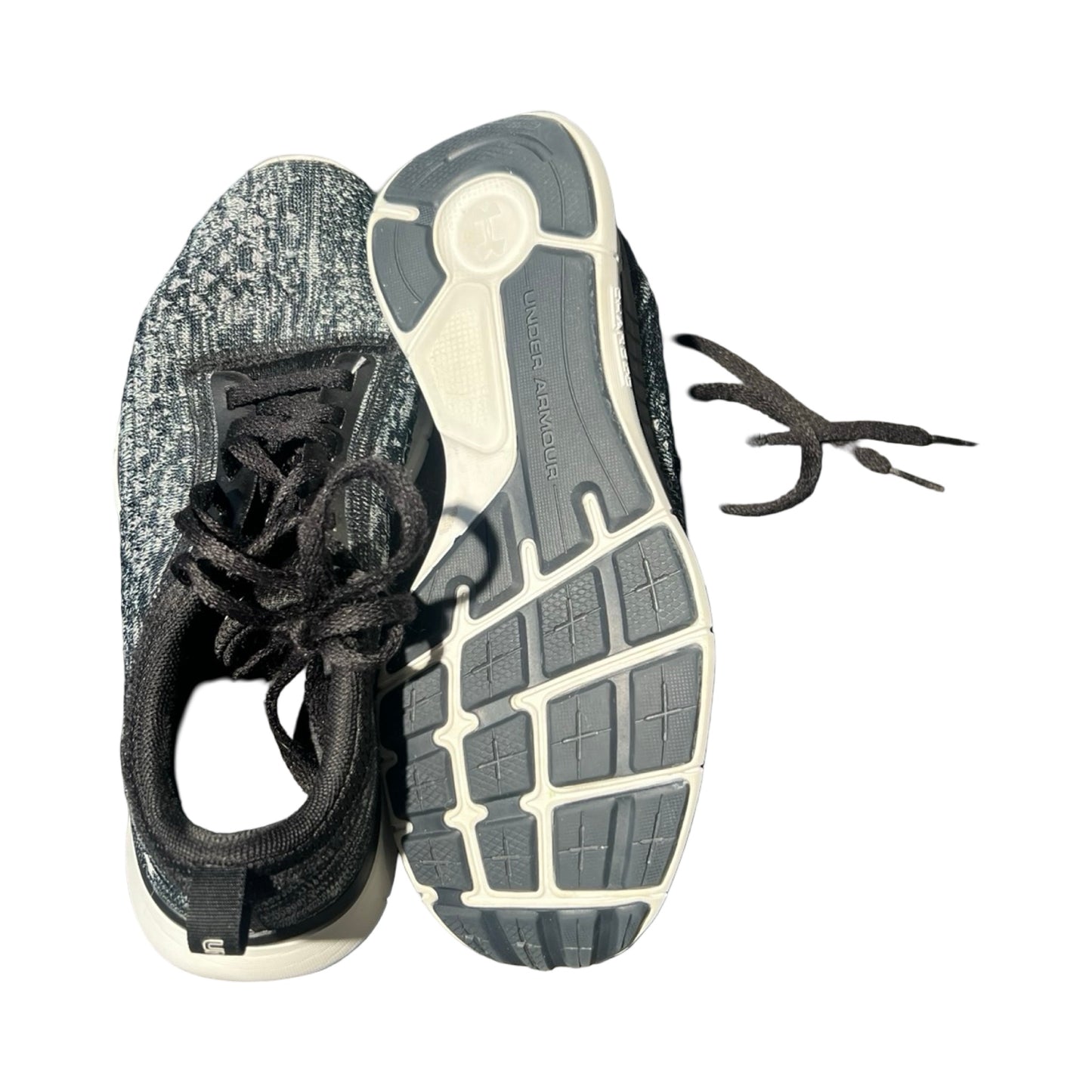 Ovansida och sula på ett par svarta och gråa träningsskor för dam från Under Armour, fotograferade mot en vit bakgrund.