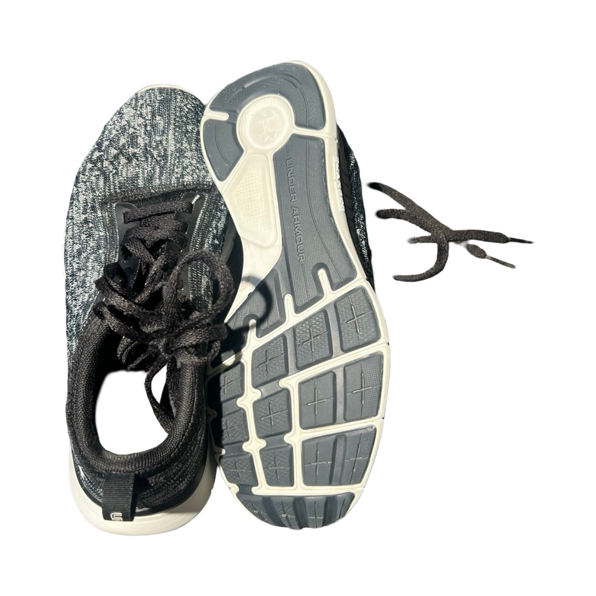 Ovansida och sula på ett par svarta och gråa träningsskor för dam från Under Armour, fotograferade mot en vit bakgrund.