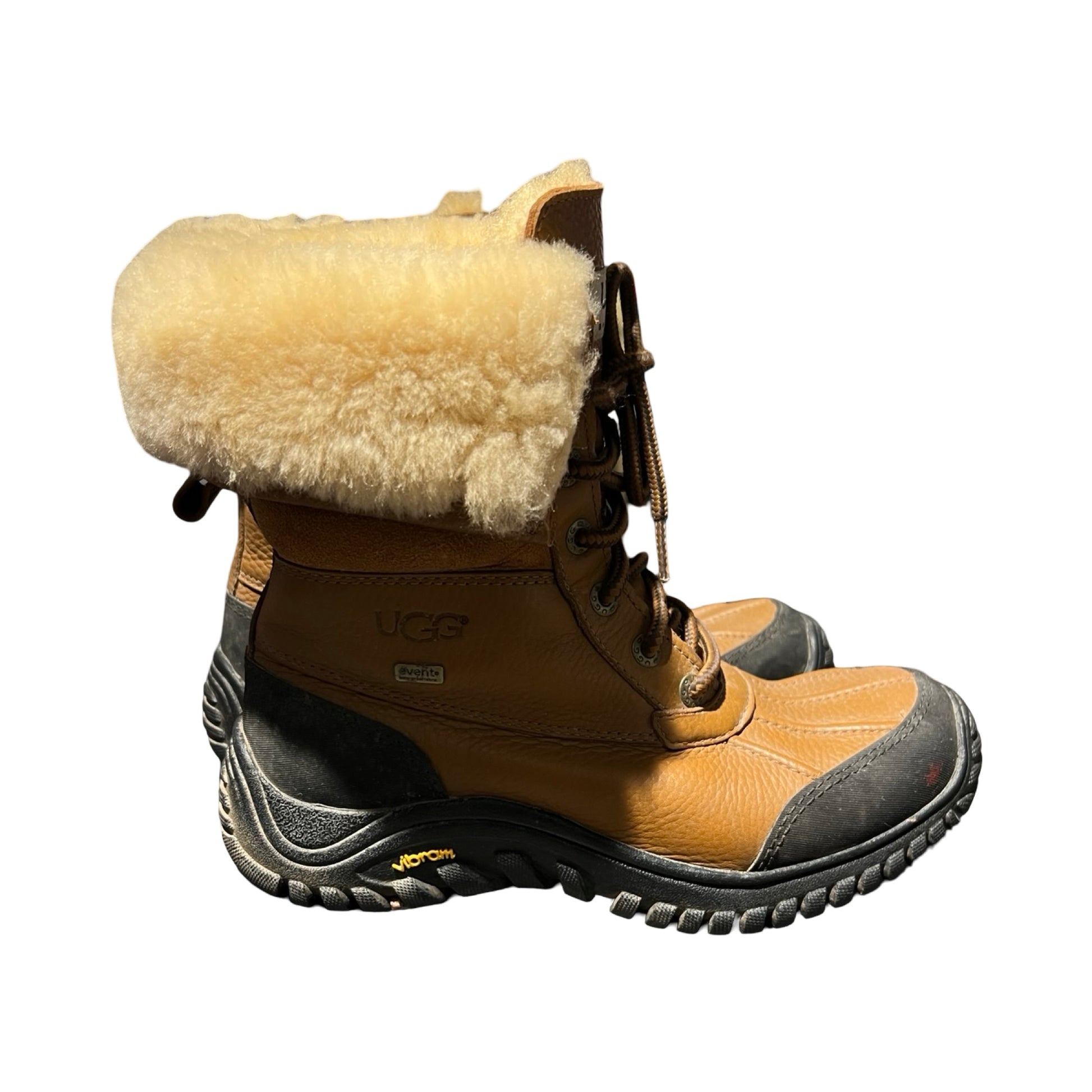 Bruna UGG vinterkängor för dam med ljust fårskinnsfoder och kraftig svart sula, fotograferade från sidan mot en vit bakgrund.