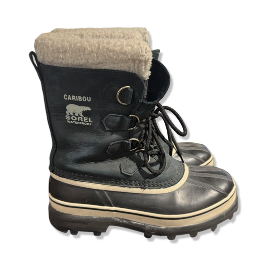 Sorel Caribou vinterkängor för dam i svart, fotograferade från sidan mot en vit bakgrund.