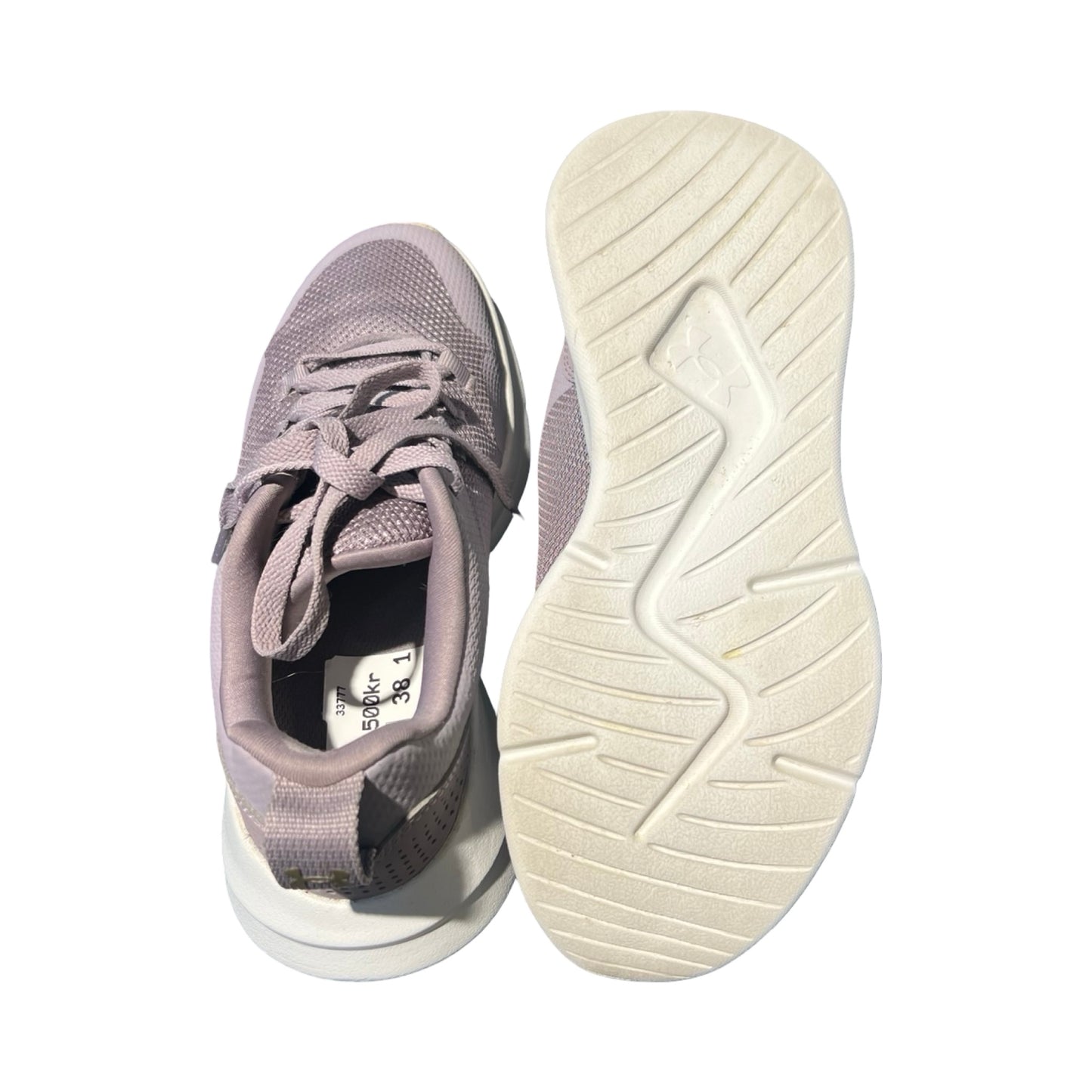 Under Armour träningsskor för dam i ljuslila. Ena skon visas uppifrån och den andra underifrån med den vita sulan synlig, fotograferat mot en vit bakgrund.