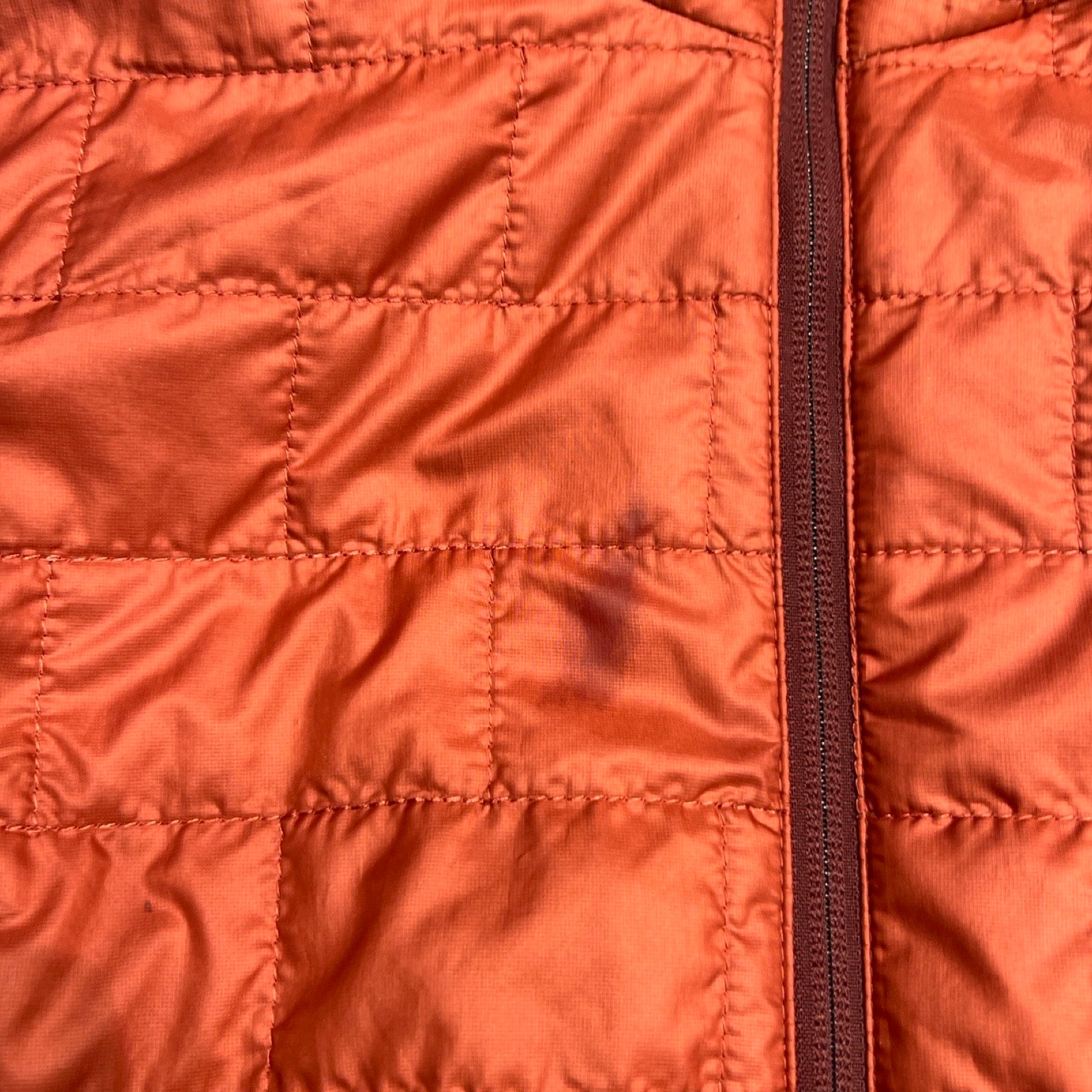 Närbild på fläcken på bröstet av den roströda syntetjackan Patagonia Nano Puff för dam.